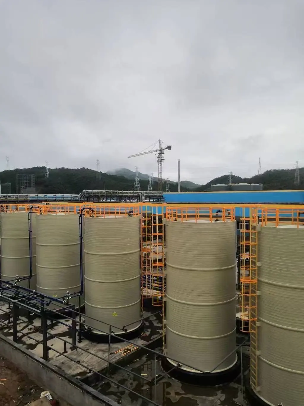 Einzügige Steigleitern mit orangefarbenem Rückenschutz an zylindrischen Lagertanks